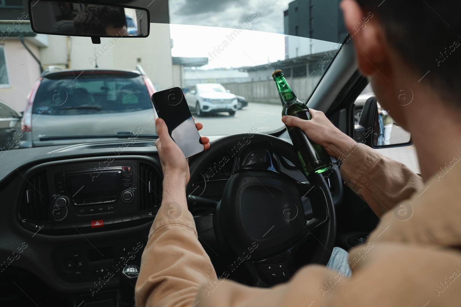 Photo of Man with bottle of beer and smartphone in car, closeup. Don't drink and drive concept