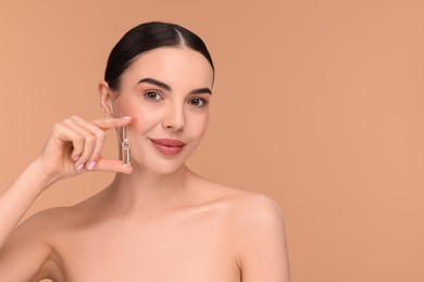 Beautiful young woman holding skincare ampoule on beige background. Space for text