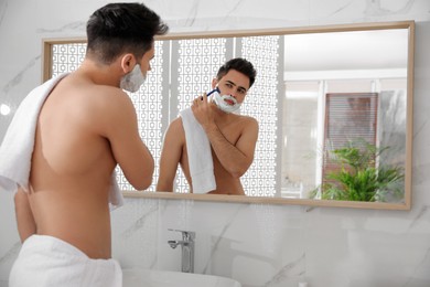 Photo of Handsome young man shaving with razor near mirror in bathroom, space for text