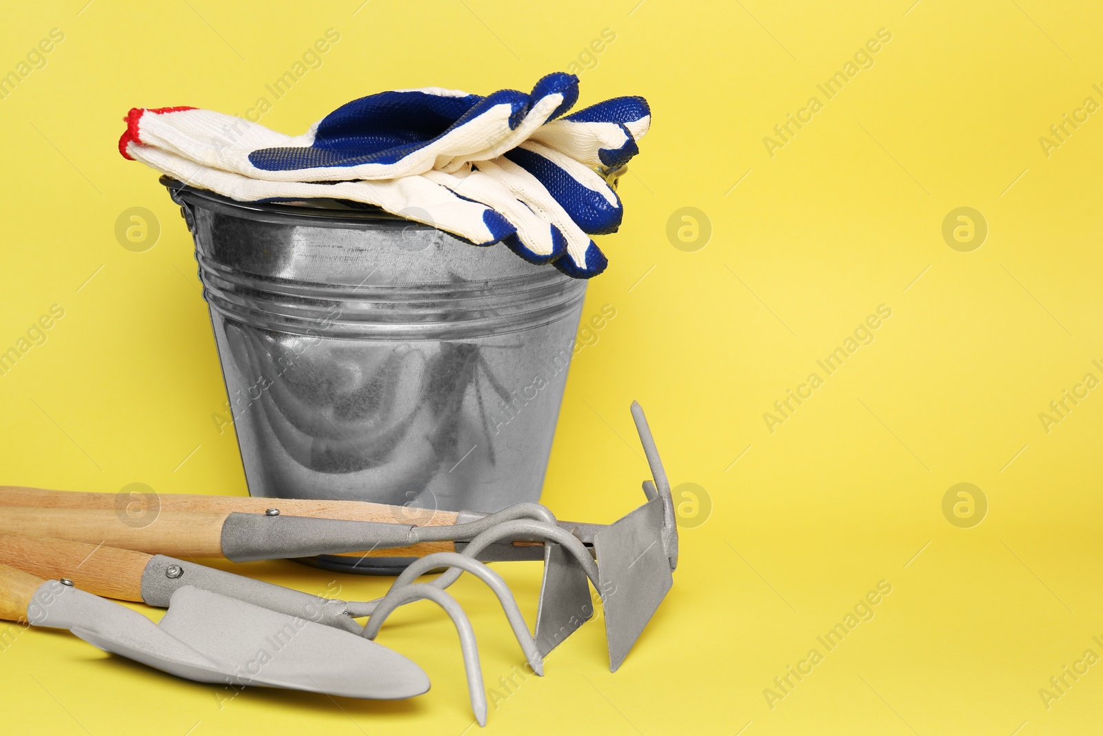 Photo of Bucket with gardening gloves and tools on yellow background. Space for text