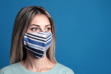 Photo of Young woman in protective face mask on blue background. Space for text