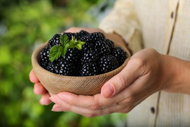 Woman holding bowl of fresh ripe blackberries on blurred natural background, closeup