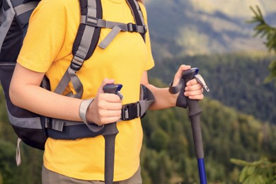 Photo of Woman with backpack and trekking poles hiking in mountains, closeup