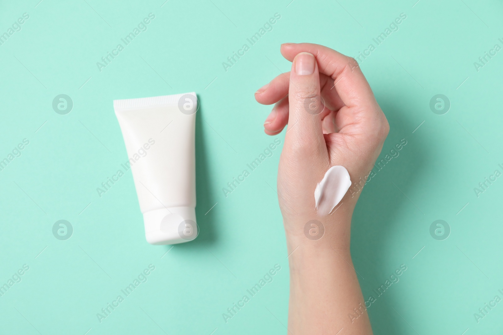 Photo of Woman with tube of hand cream on turquoise background, top view