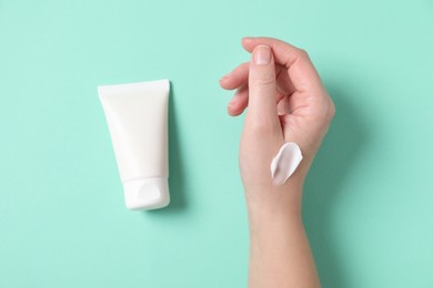 Woman with tube of hand cream on turquoise background, top view