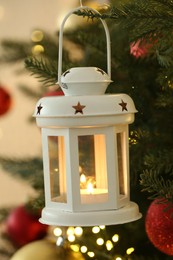 Christmas lantern with burning candle on fir tree against blurred background, closeup