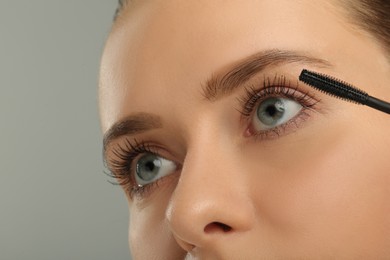 Woman applying mascara on grey background, closeup