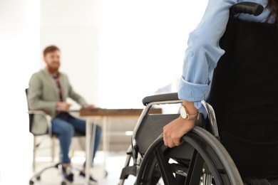 Photo of Young woman in wheelchair with colleague at office, closeup