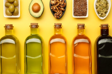 Vegetable fats. Different oils in glass bottles and ingredients on yellow table, flat lay