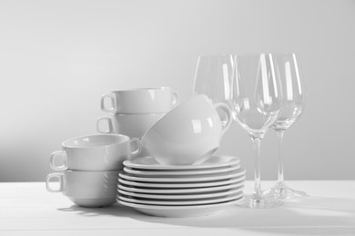 Set of clean dishware and glasses on white wooden table against light background