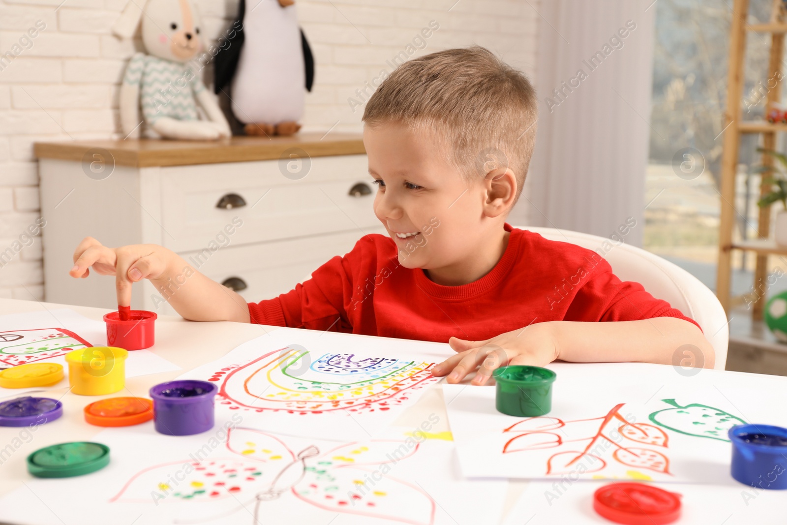 Photo of Little boy painting with finger at white table indoors