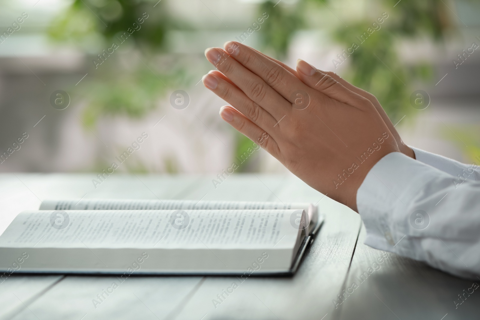 Photo of Woman holding hands clasped while praying at grey wooden table with Bible, closeup