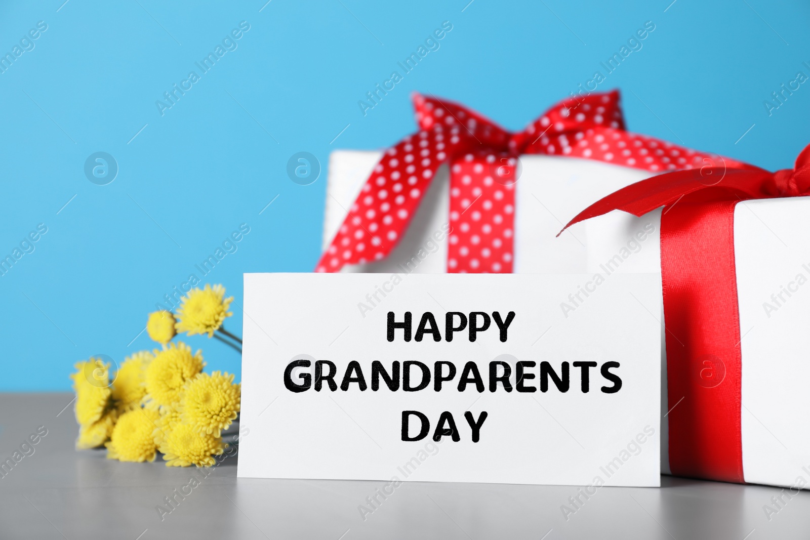 Photo of Card with phrase Happy Grandparents Day, gift boxes and beautiful flowers on grey table