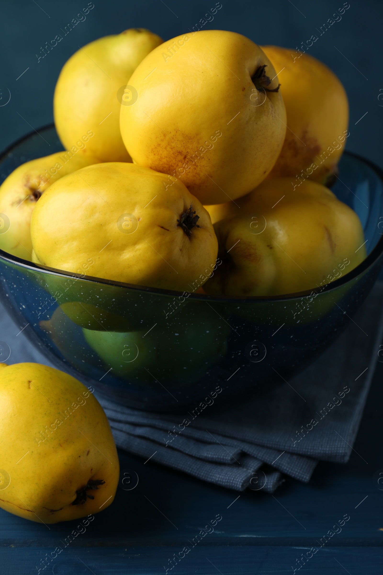 Photo of Tasty ripe quinces in bowl on blue wooden table, closeup