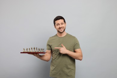 Photo of Handsome man pointing at chessboard with game pieces on light grey background