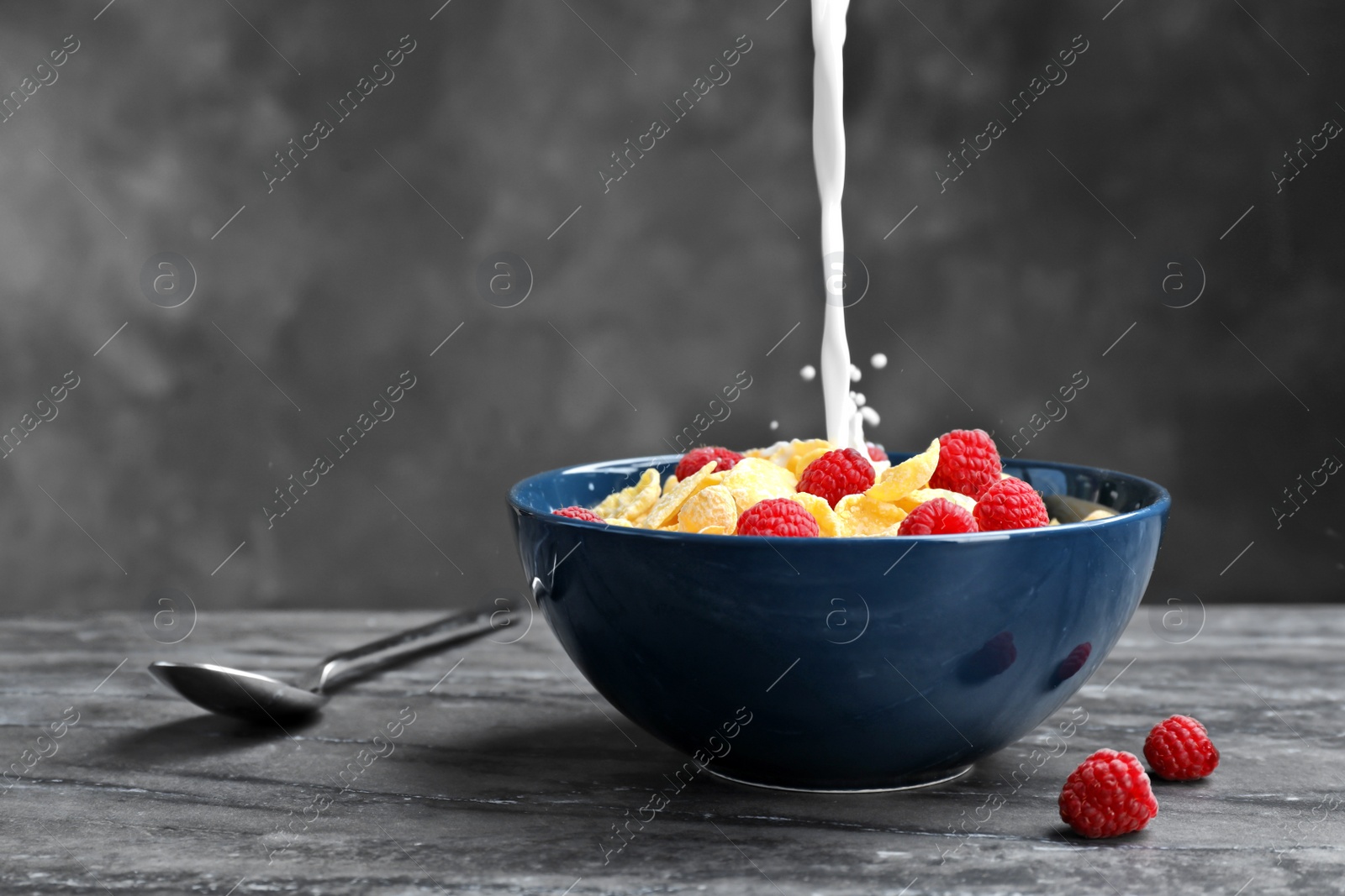 Photo of Pouring milk into bowl with cornflakes on dark table. Whole grain cereal for breakfast