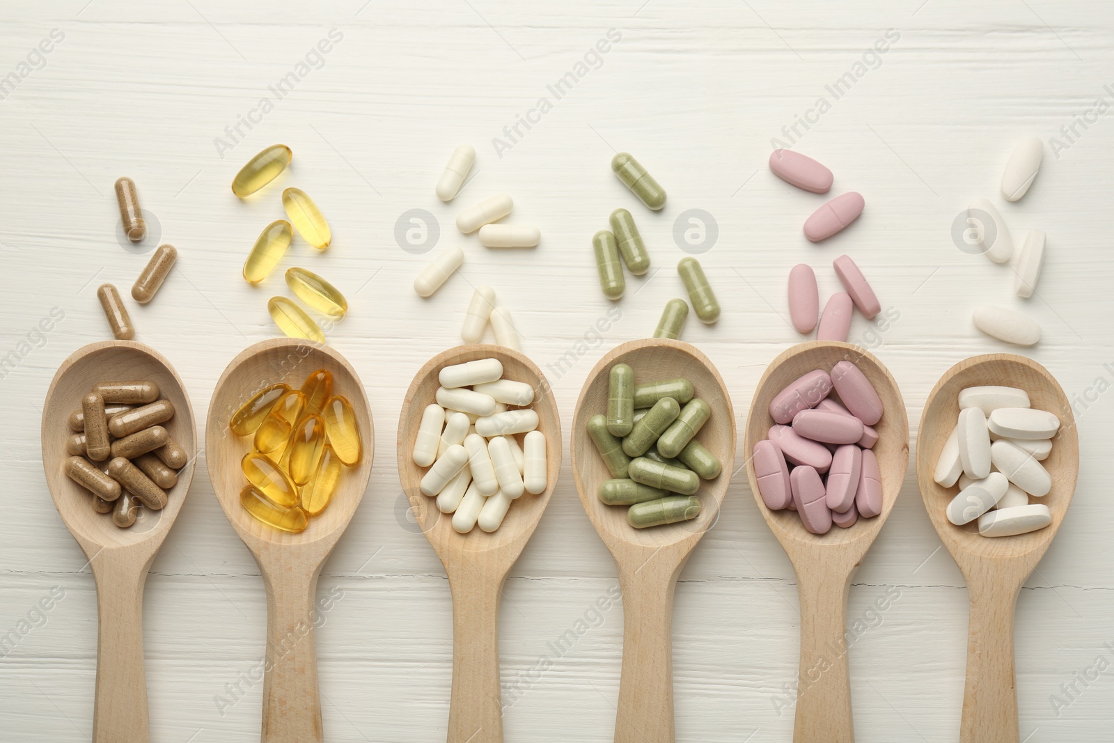 Photo of Different vitamin capsules in spoons on white wooden table, flat lay