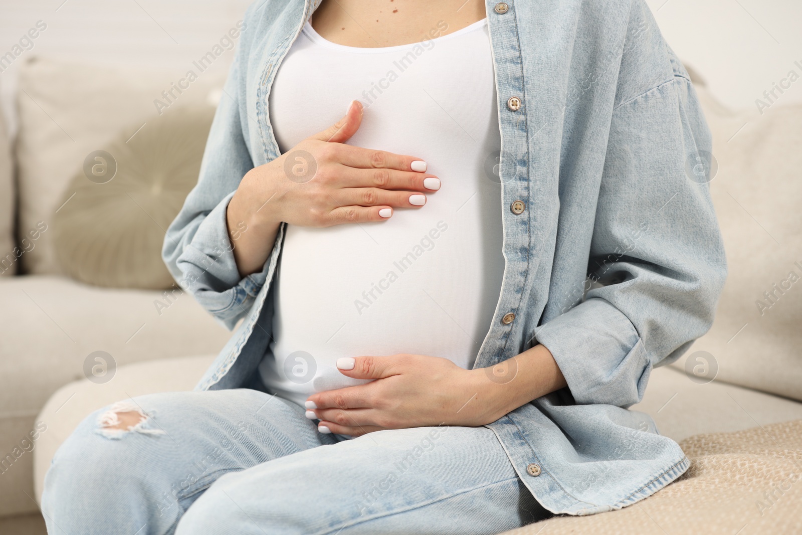 Photo of Pregnant woman touching her belly on sofa at home, closeup