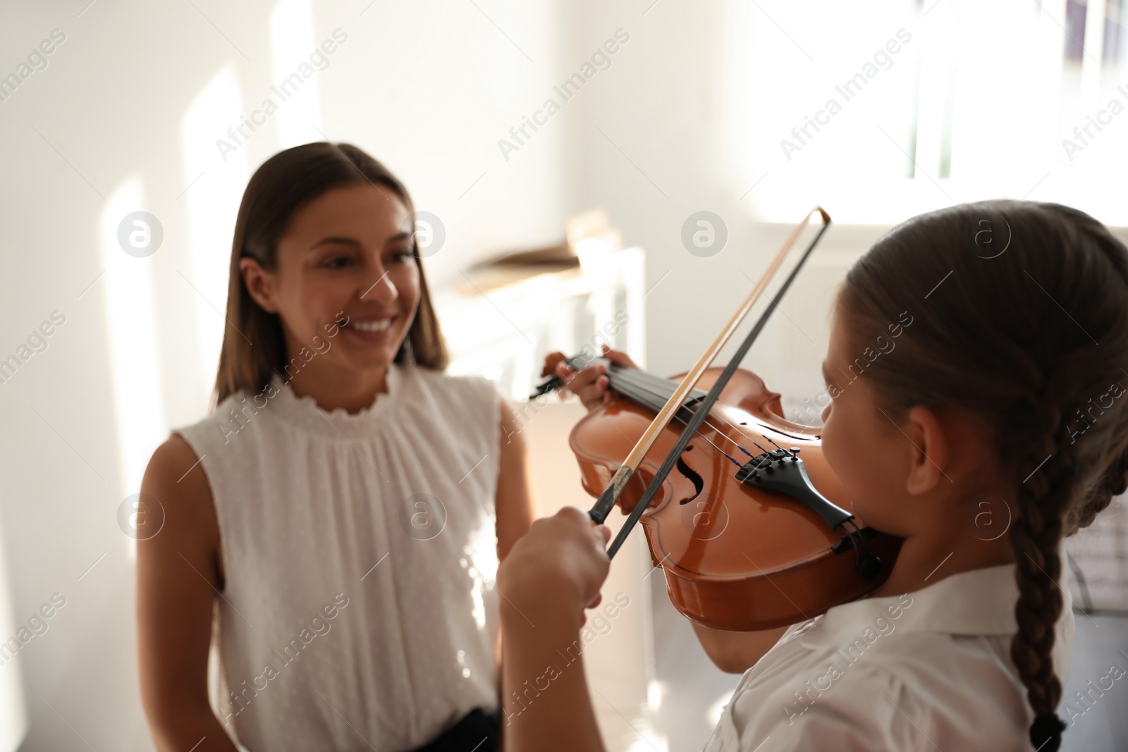 Photo of Young woman teaching little girl to play violin indoors