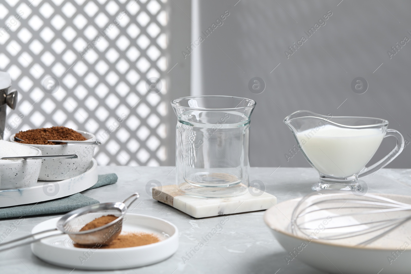 Photo of Empty glass, milk, sieve with cinnamon powder and instant granules on light gray table. Making dalgona coffee