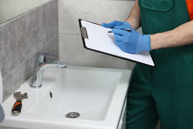 Plumber writing results of examining sink in bathroom, closeup