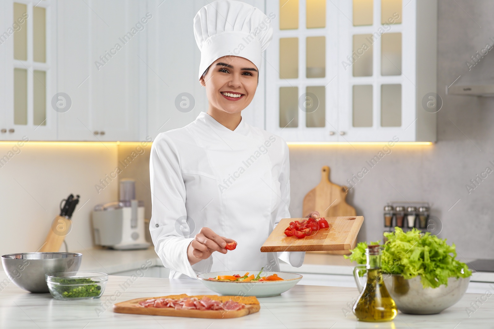 Photo of Professional chef adding cut tomato into delicious salad at white marble table in kitchen