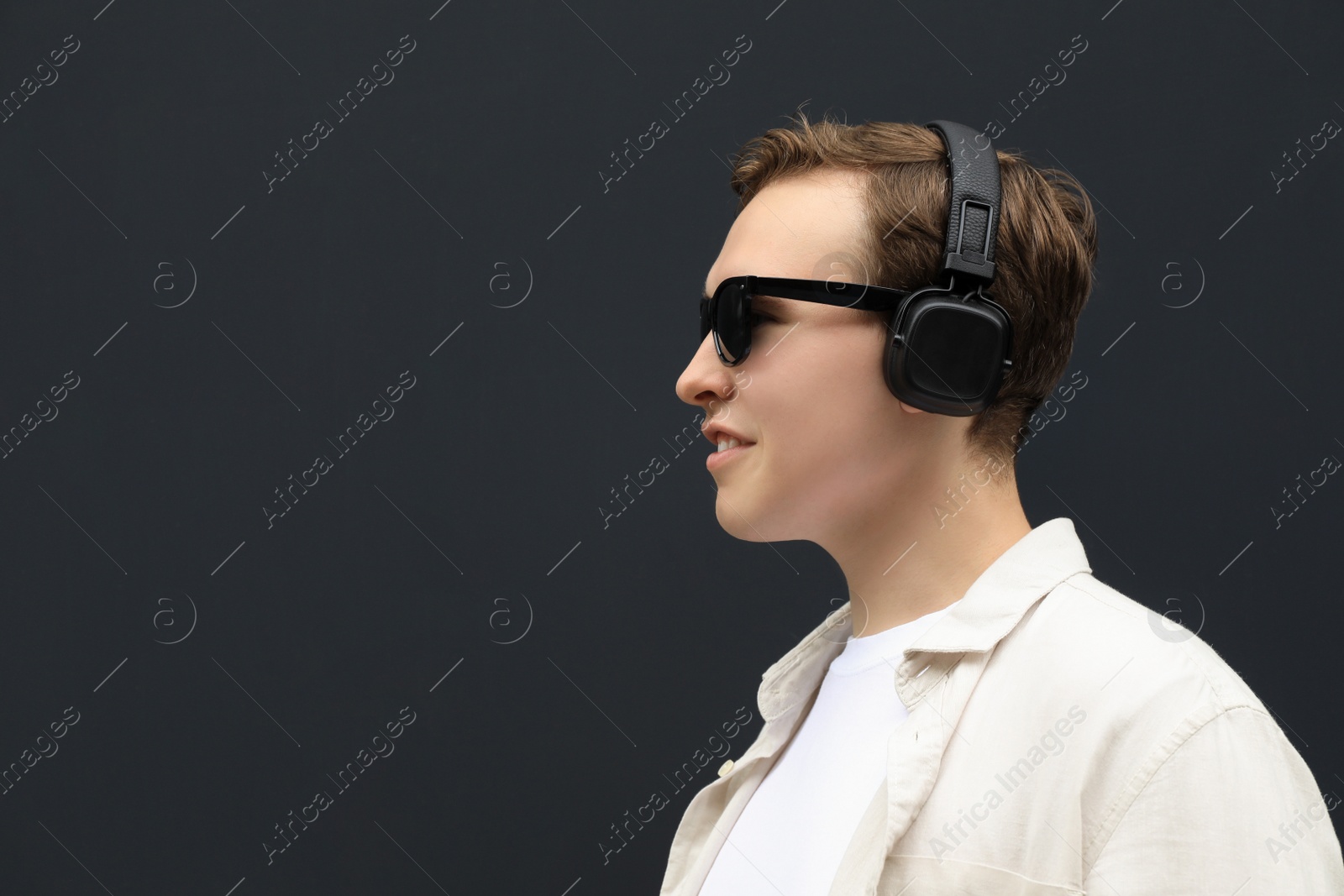 Photo of Handsome young man with headphones near black wall. Space for text