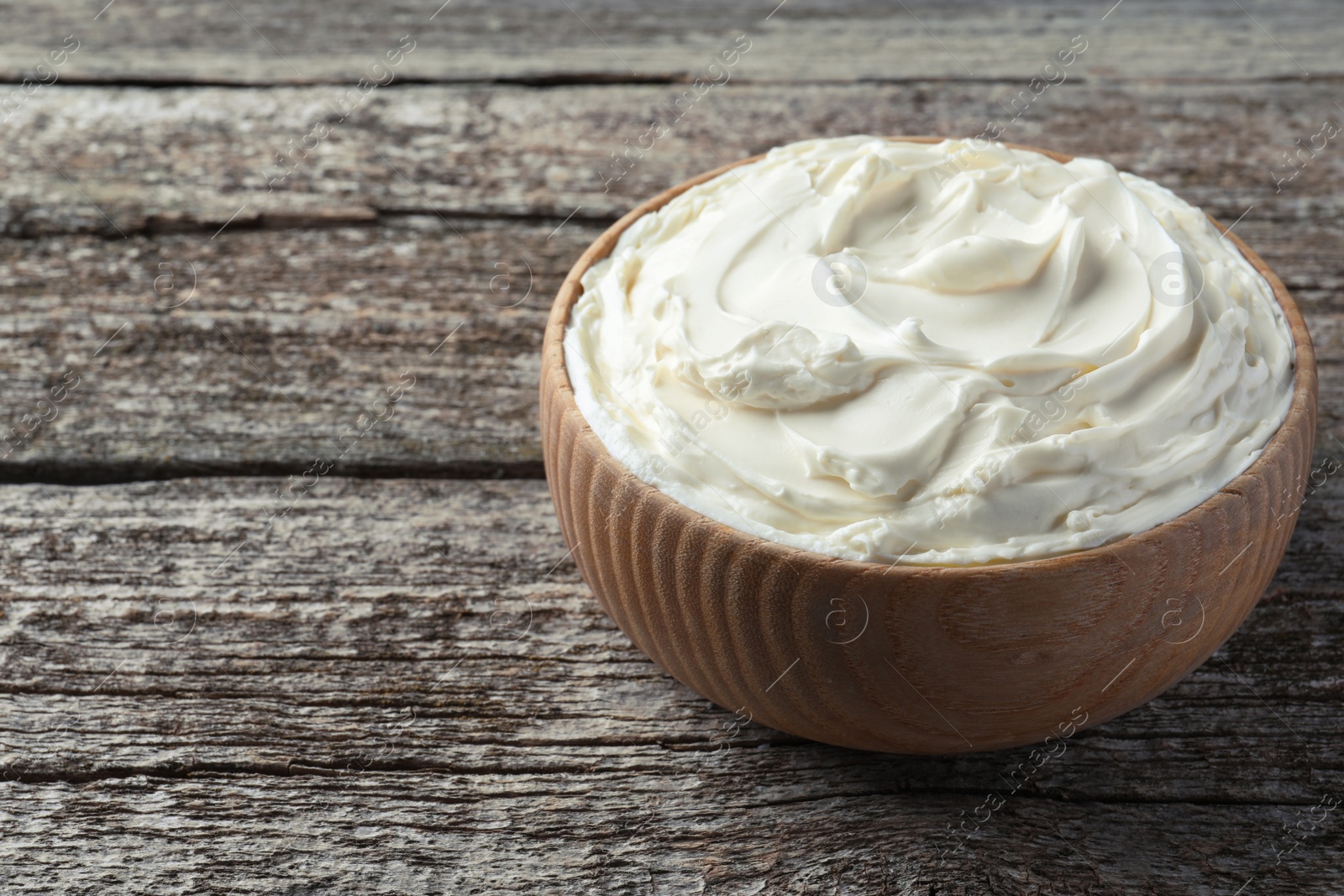 Photo of Bowl of tasty cream cheese on wooden table, space for text