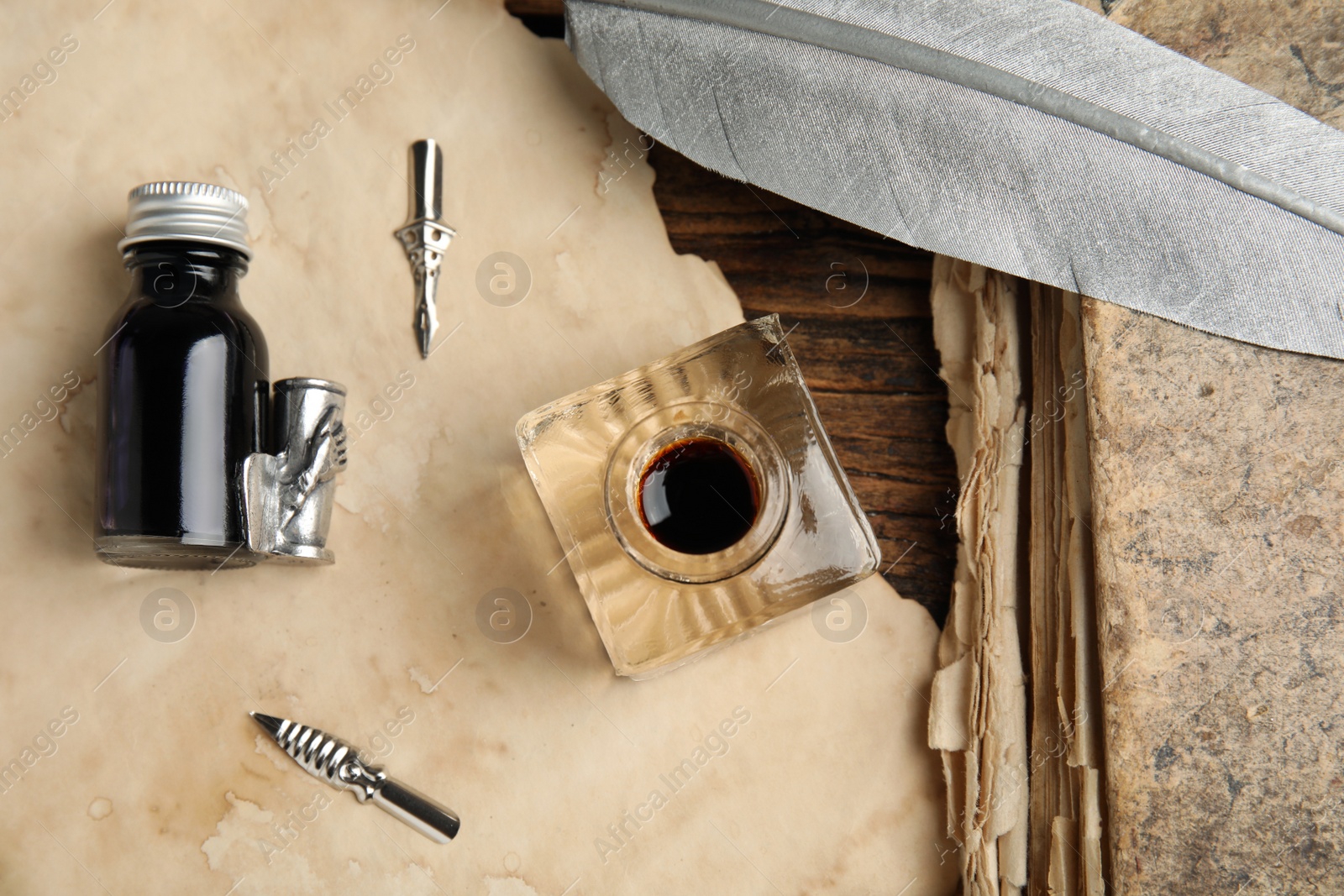 Photo of Feather pen, inkwell and paper on wooden table, flat lay