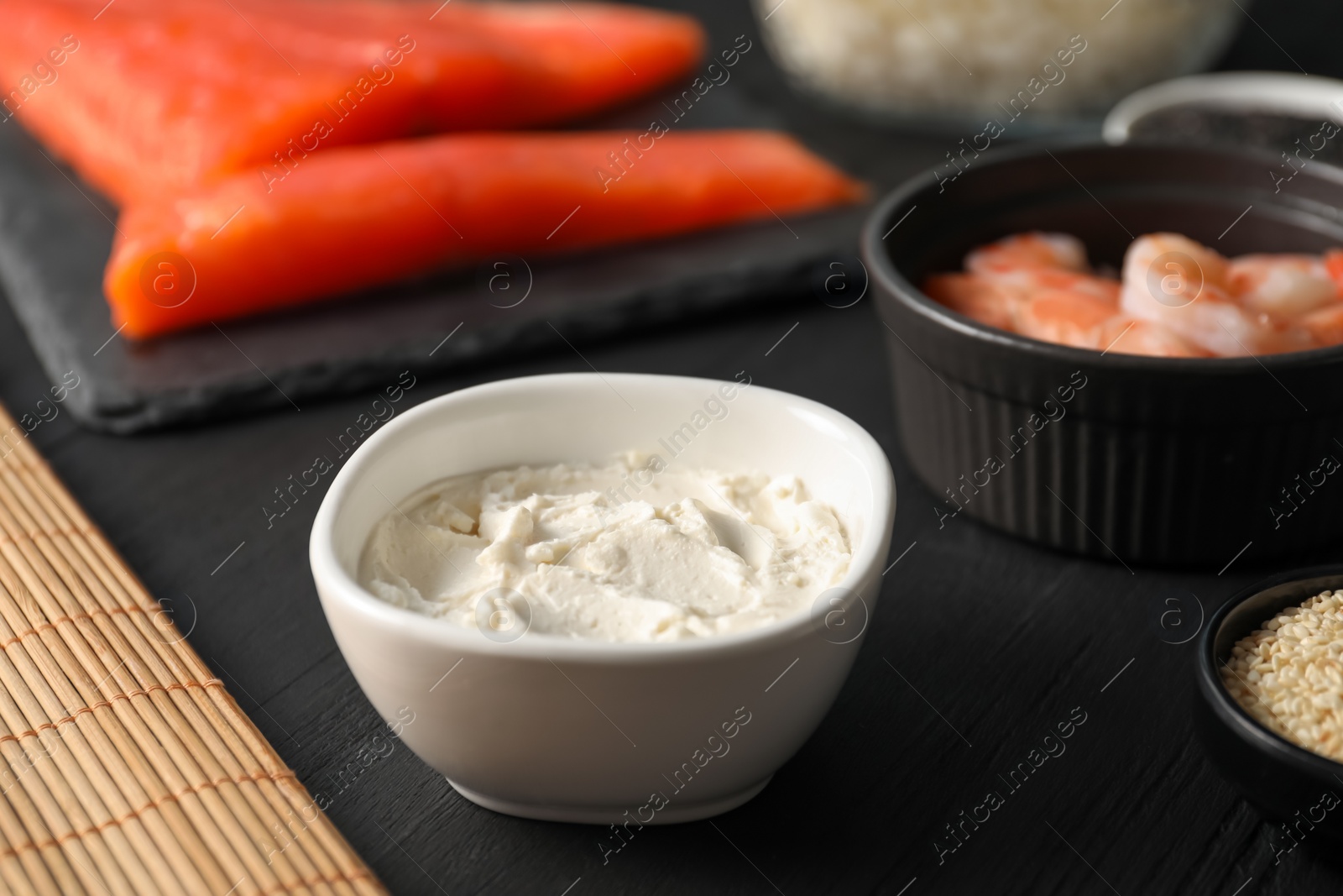 Photo of Cream cheese in bowl and other ingredients for sushi on black table, closeup