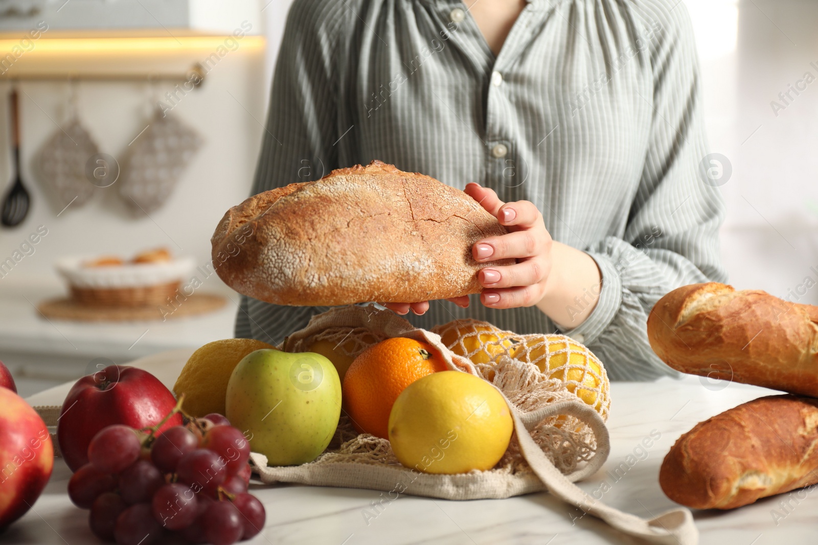 Photo of Woman bread and string bag of fresh fruits at light marble table, closeup