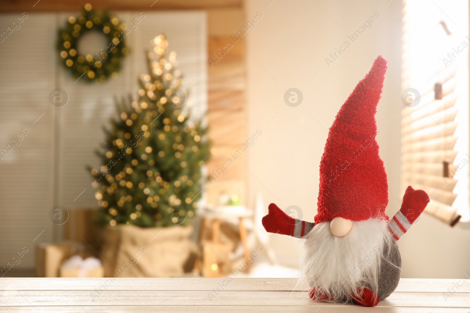 Image of Funny Christmas gnome on white wooden table in room with festive decorations. Space for text