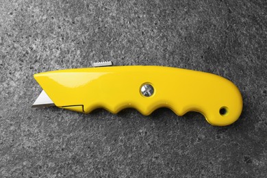 Photo of Yellow utility knife on grey table, top view. Construction tool