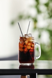 Mason jar of cola with ice on table against blurred background