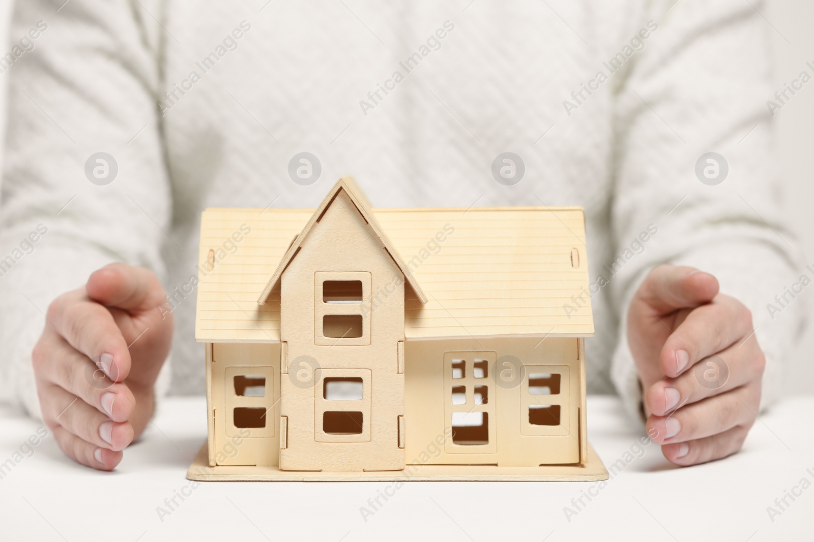 Photo of Home security concept. Man with house model at white table, closeup