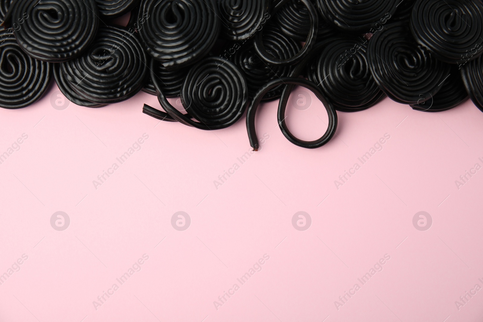 Photo of Tasty black liquorice candies on pink background, flat lay. Space for text