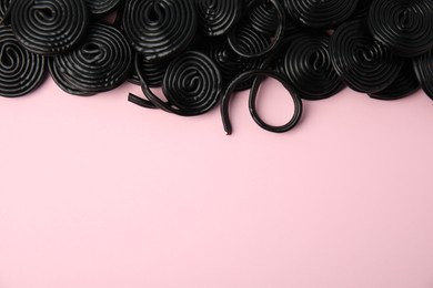 Tasty black liquorice candies on pink background, flat lay. Space for text