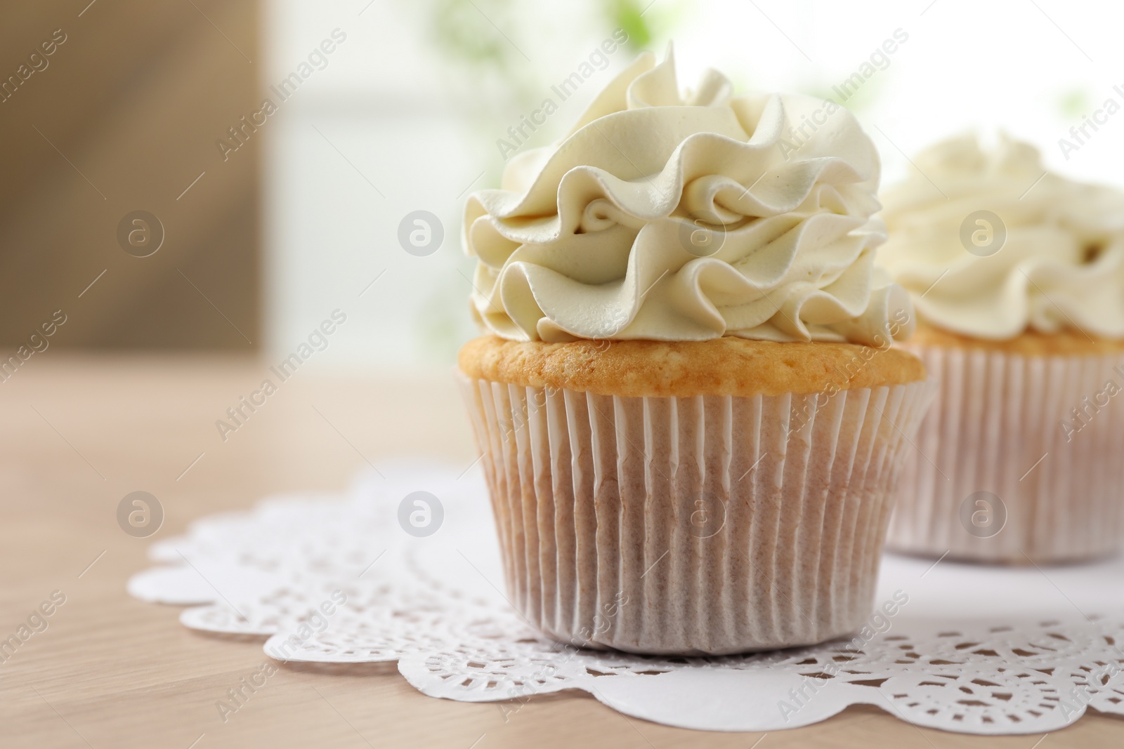 Photo of Tasty cupcakes with vanilla cream on light wooden table, closeup