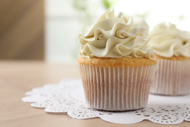 Photo of Tasty cupcakes with vanilla cream on light wooden table, closeup