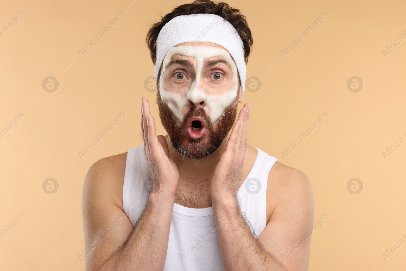 Photo of Emotional man with headband washing his face on beige background