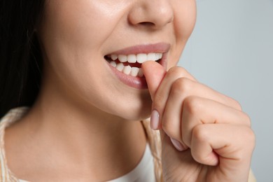 Photo of Young woman biting her nails on light grey background, closeup