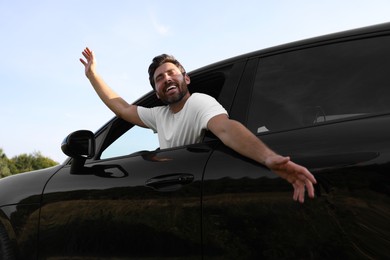 Enjoying trip. Happy man leaning out of car window outdoors, low angle view