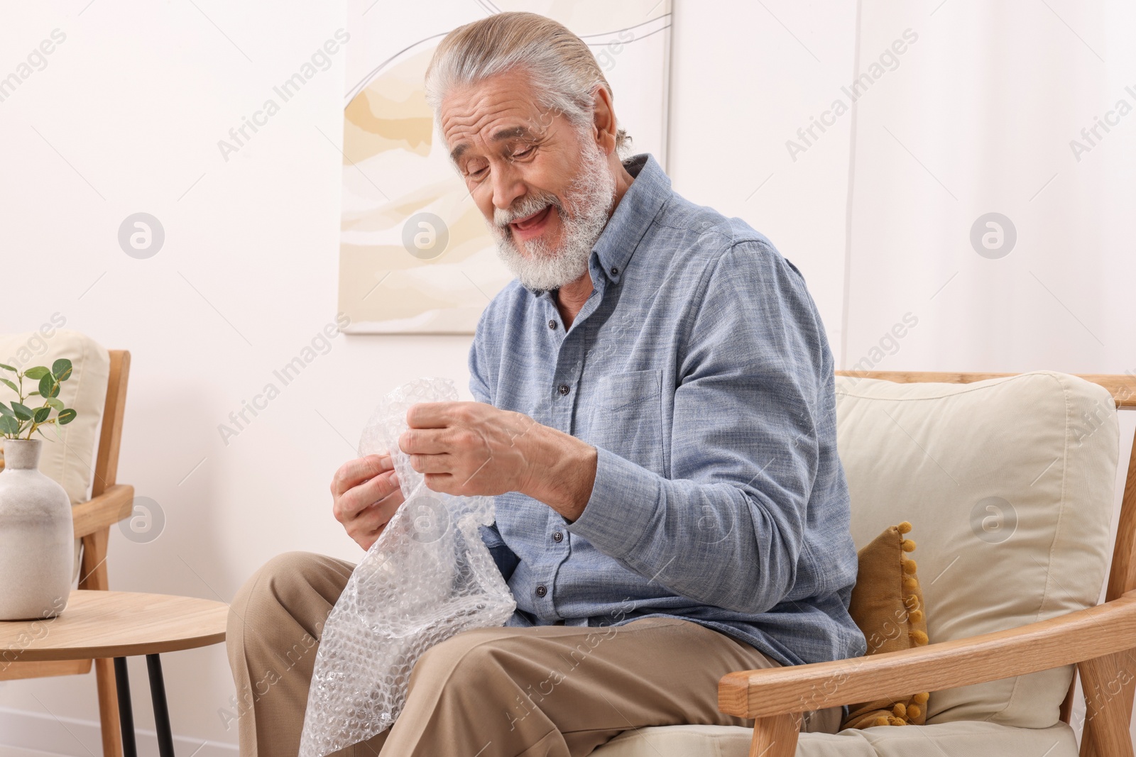 Photo of Senior man popping bubble wrap at home. Stress relief
