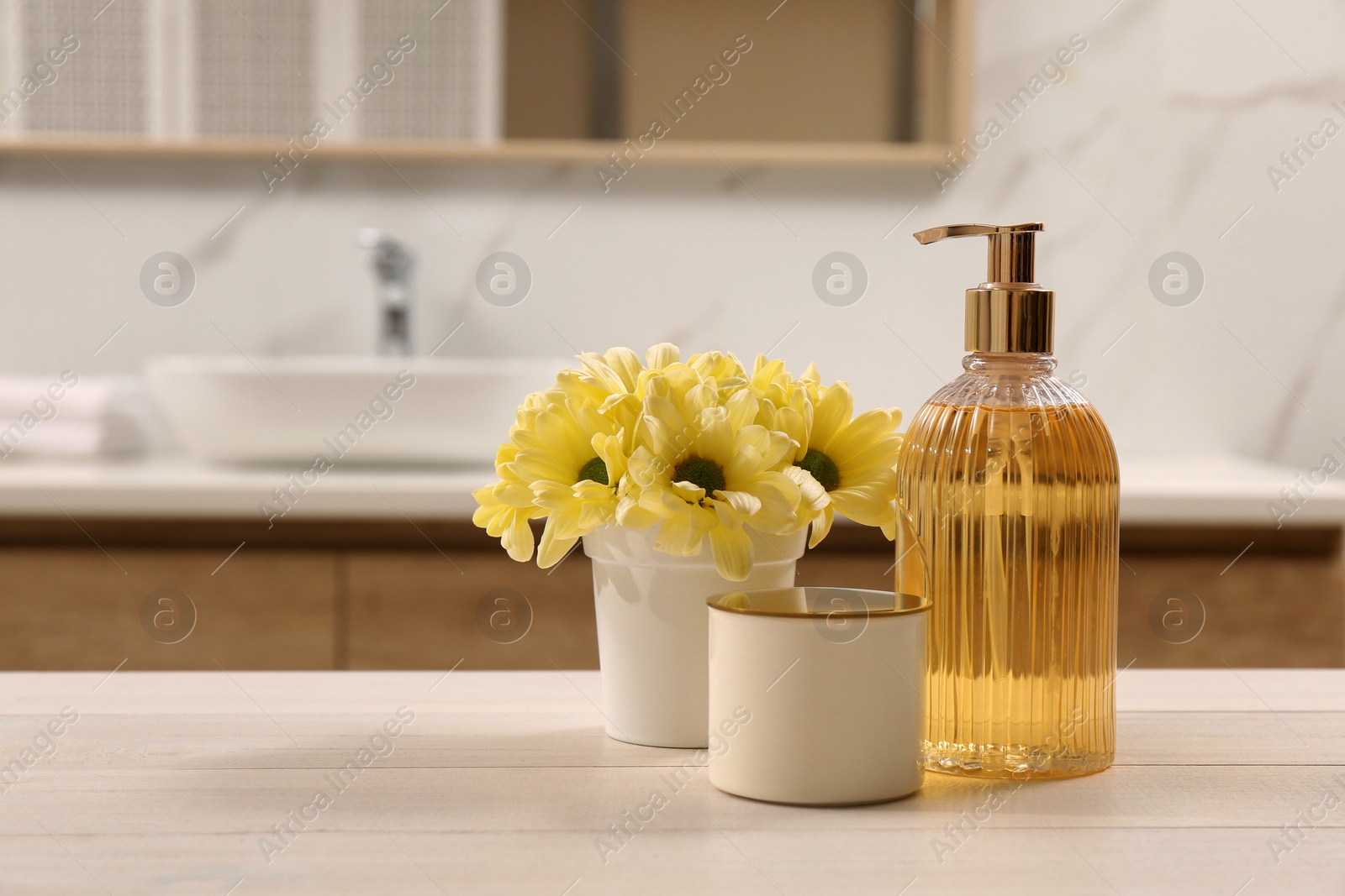 Photo of Glass dispenser with liquid soap, candle holder and beautiful flowers on white table in bathroom, space for text