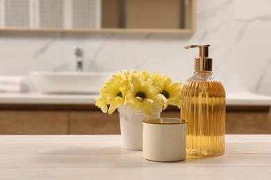 Photo of Glass dispenser with liquid soap, candle holder and beautiful flowers on white table in bathroom, space for text
