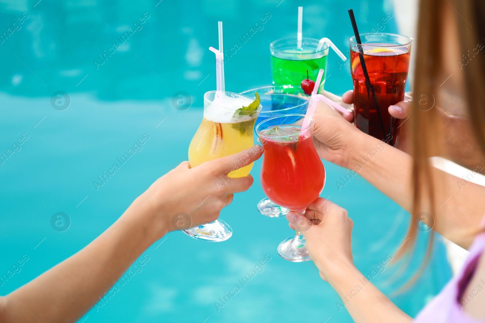 Photo of Friends clinking glasses with fresh summer cocktails near swimming pool, closeup