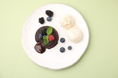Photo of Plate with delicious chocolate fondant, berries, mint and ice cream on light green table, top view
