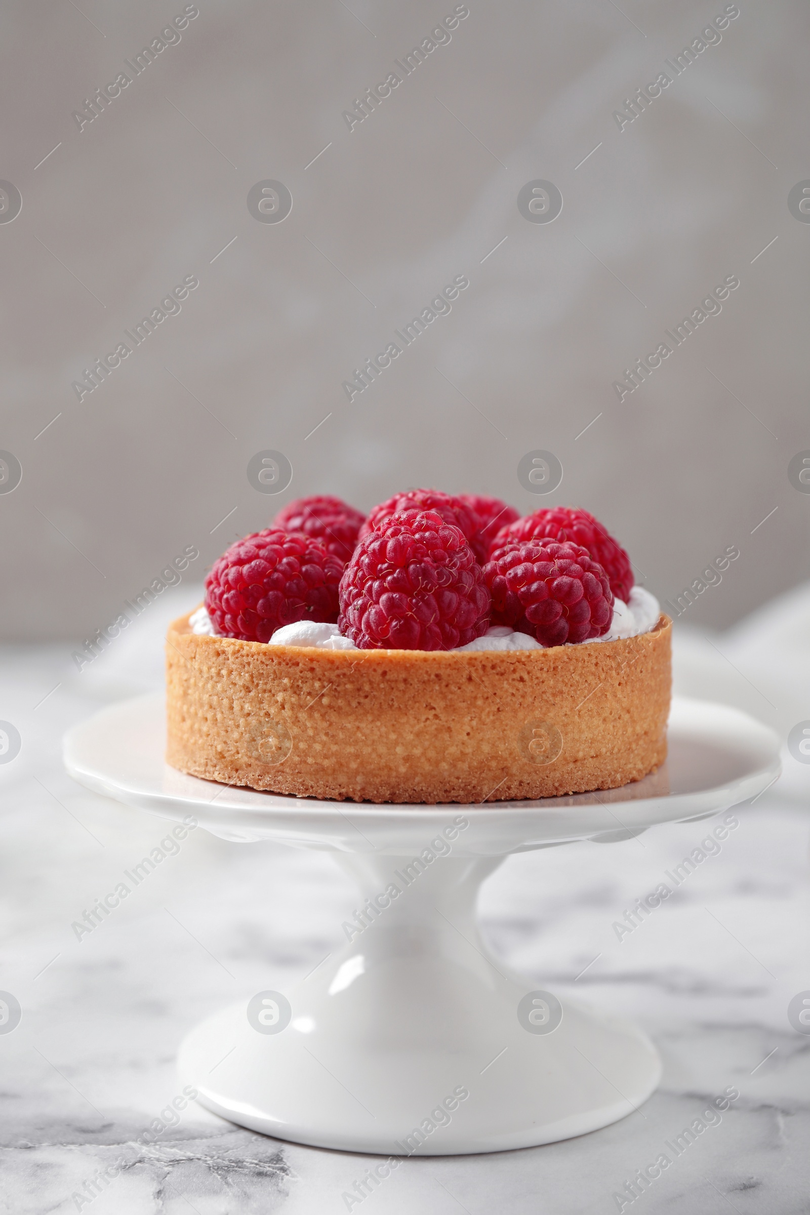 Photo of Cake stand with raspberry tart on marble table against light background. Delicious pastries