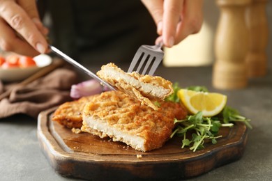 Photo of Woman eating delicious schnitzel with microgreens and lemon at grey table, closeup