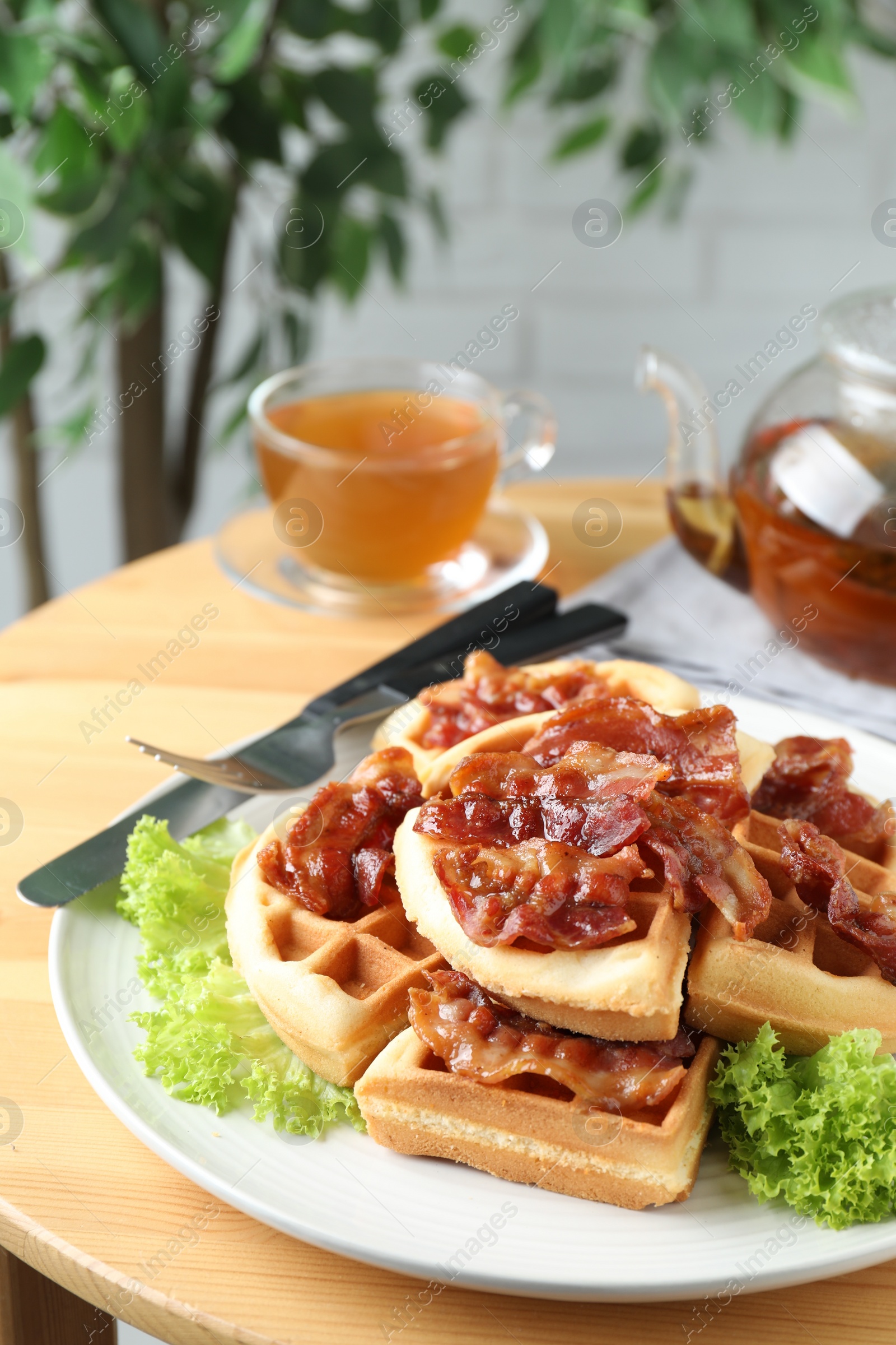 Photo of Tasty Belgian waffles served with bacon, lettuce and tea on wooden table, closeup